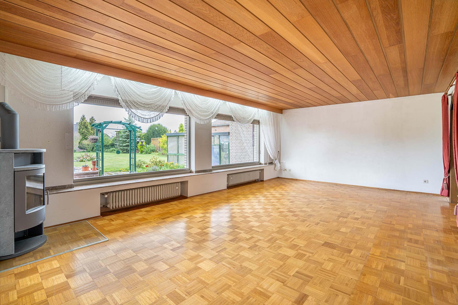 Blick aus der Diele in das Wohnzimmer mit großen Fenstern und Blick in den Garten, Kamin und offenem Rundbogen in die Wohnküche. Immobilie Bedburg