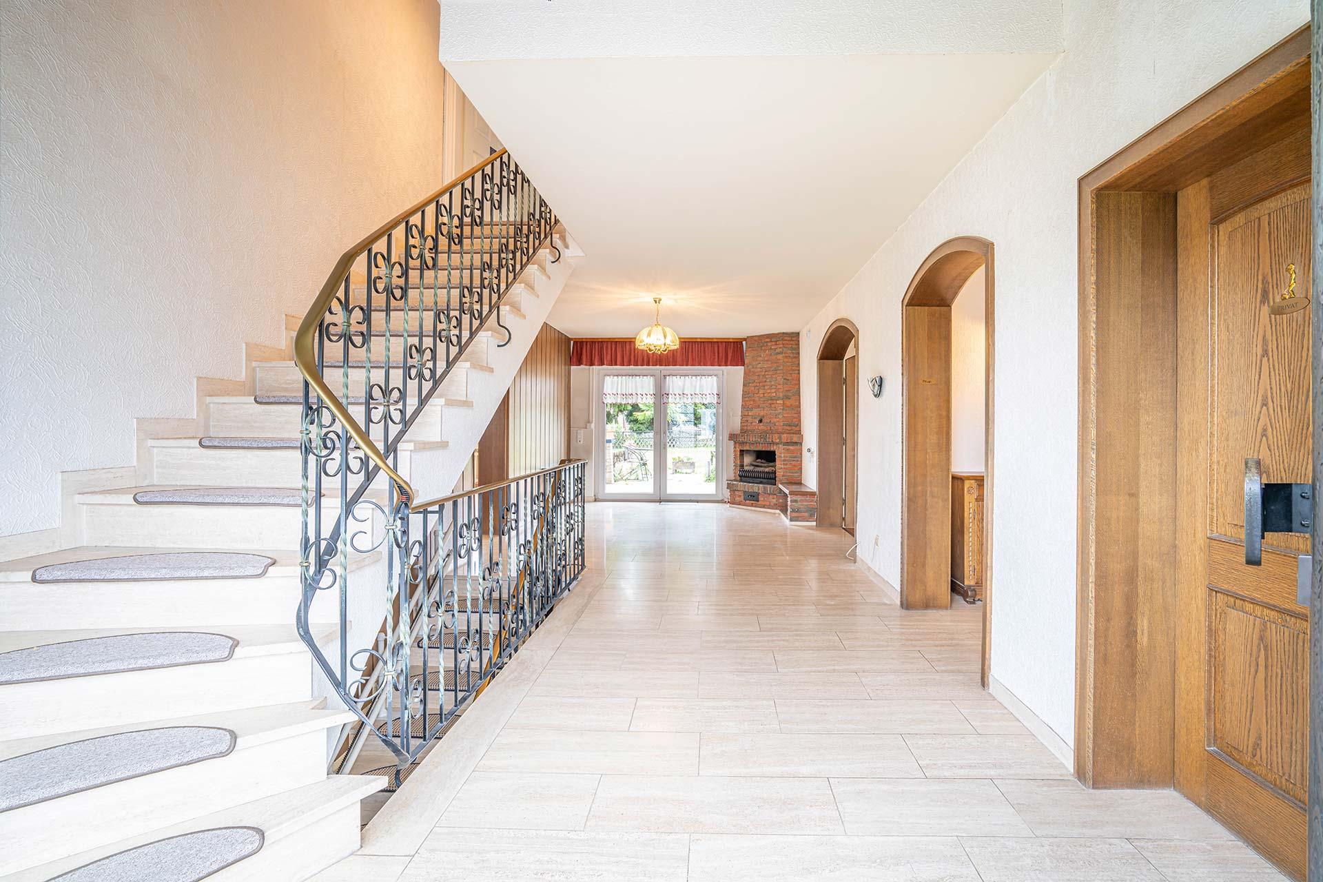 Blick in die Eingangshalle im Erdgeschoss mit Rundbogenflügeltür, offenem Kamin und eleganter Treppe ins Dachgeschoss. Immobilie Bedburg