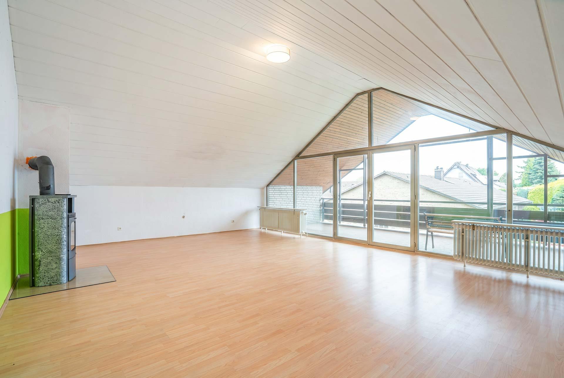 Blick in das Wohn- und Esszimmer im Dachgeschoss mit Kamin und Zugang zur Loggia. Immobilie Bedburg