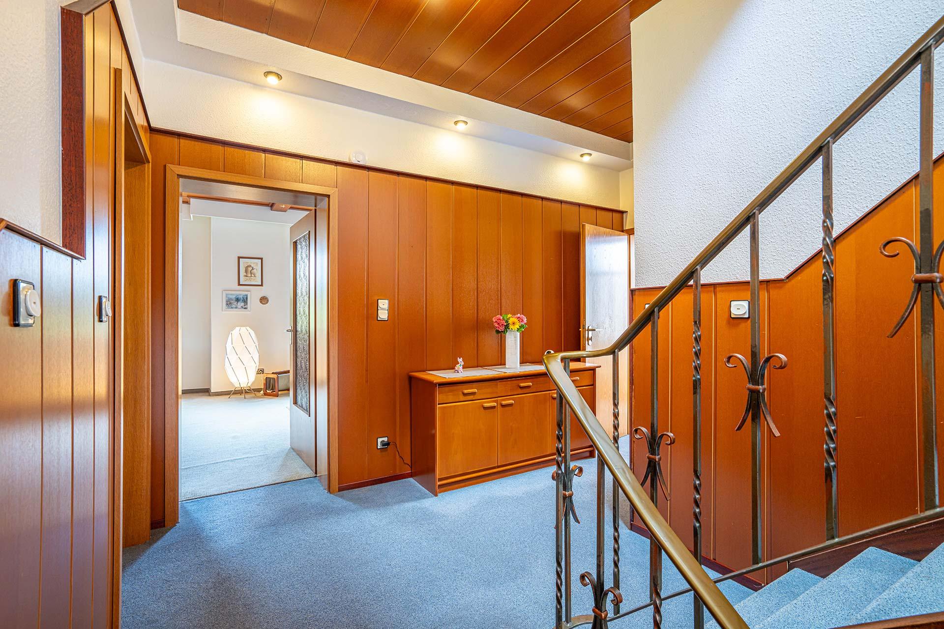 Blick aus dem offenen Treppenhaus in den Flur der Wohnung im Obergeschoss mit Zugängen zu Küche, Wohn- und Esszimmer, Arbeitszimmer und Gäste WC. Die Treppe führt weiter ins Obergeschoss zu den Schlafzimmer. Immobilie Bedburg