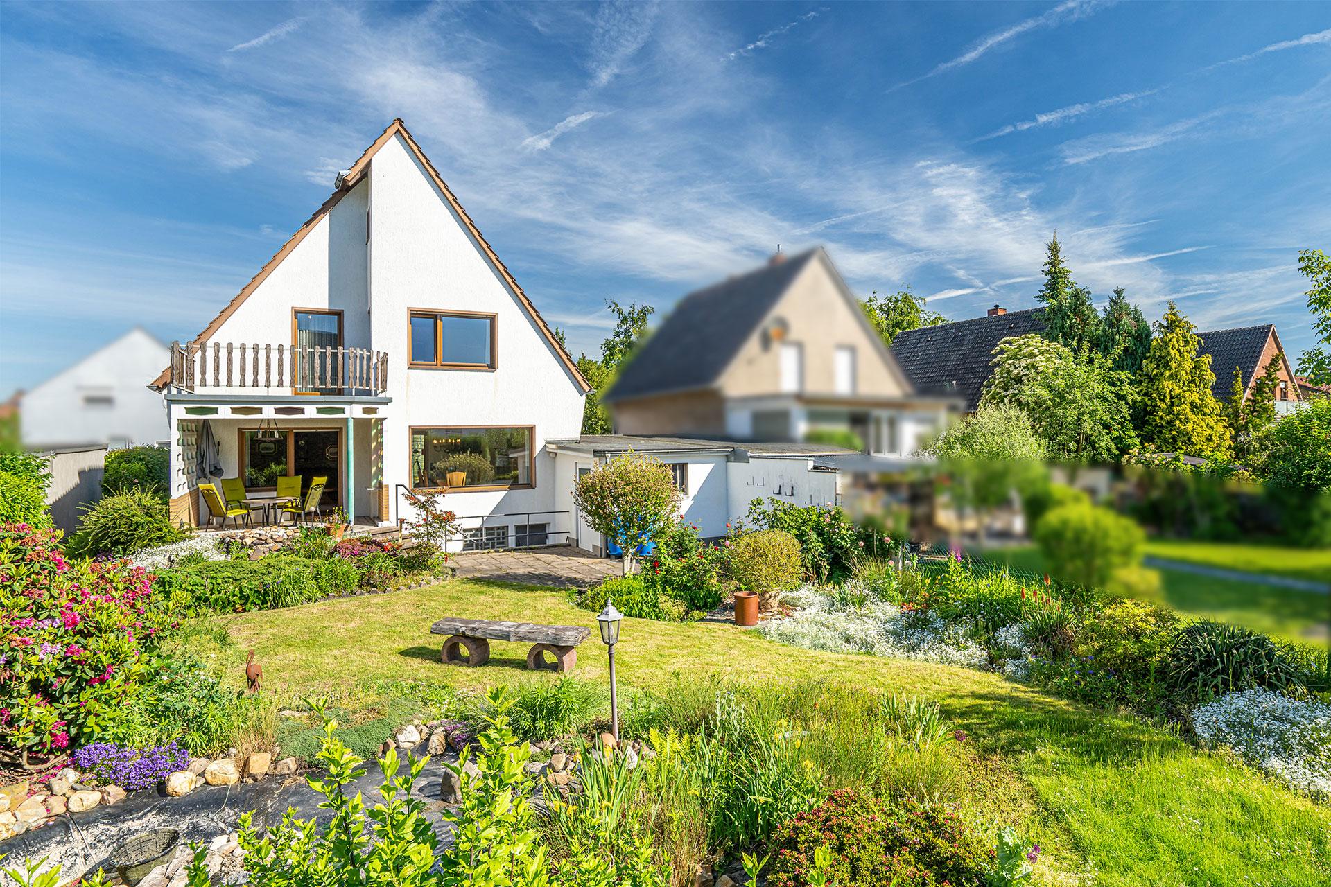 Blick auf die Immobilie mit der Terrasse, der Garage und dem blühenden Garten mit Azaleen, Rosen und vielen anderen weißen und lila blühenden Blumen, den Gartenteich und Rasenfläche. Einfamilienhaus Bergheim